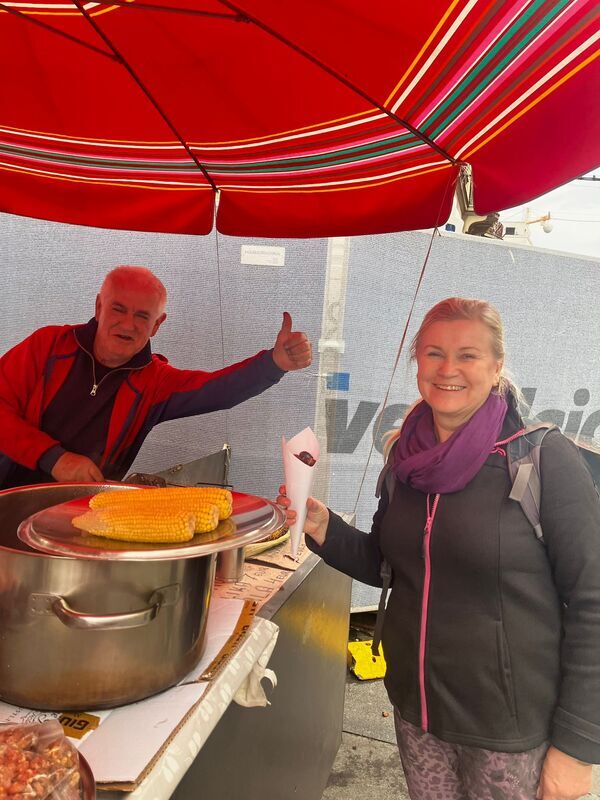 1000014677.jpg A woman at a street stall where a man is grilling corn on the cob.