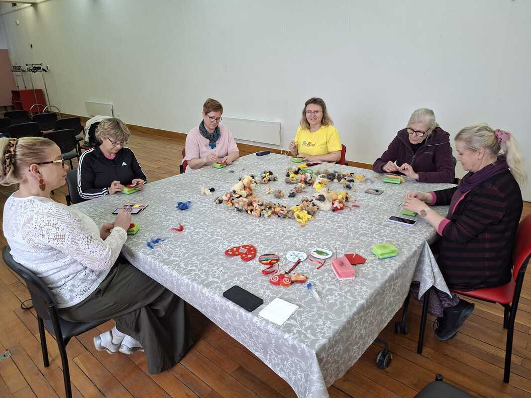 1000014741.jpg A group of women doing wool handicrafts around a table.