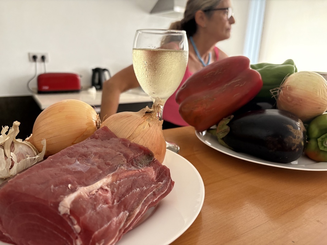 Viinilasi sekä tuoreet raaka-aineet, liha ja kasvikset, ovat valmiina pöydällä odottamassa ruuanlaiton alkamista.