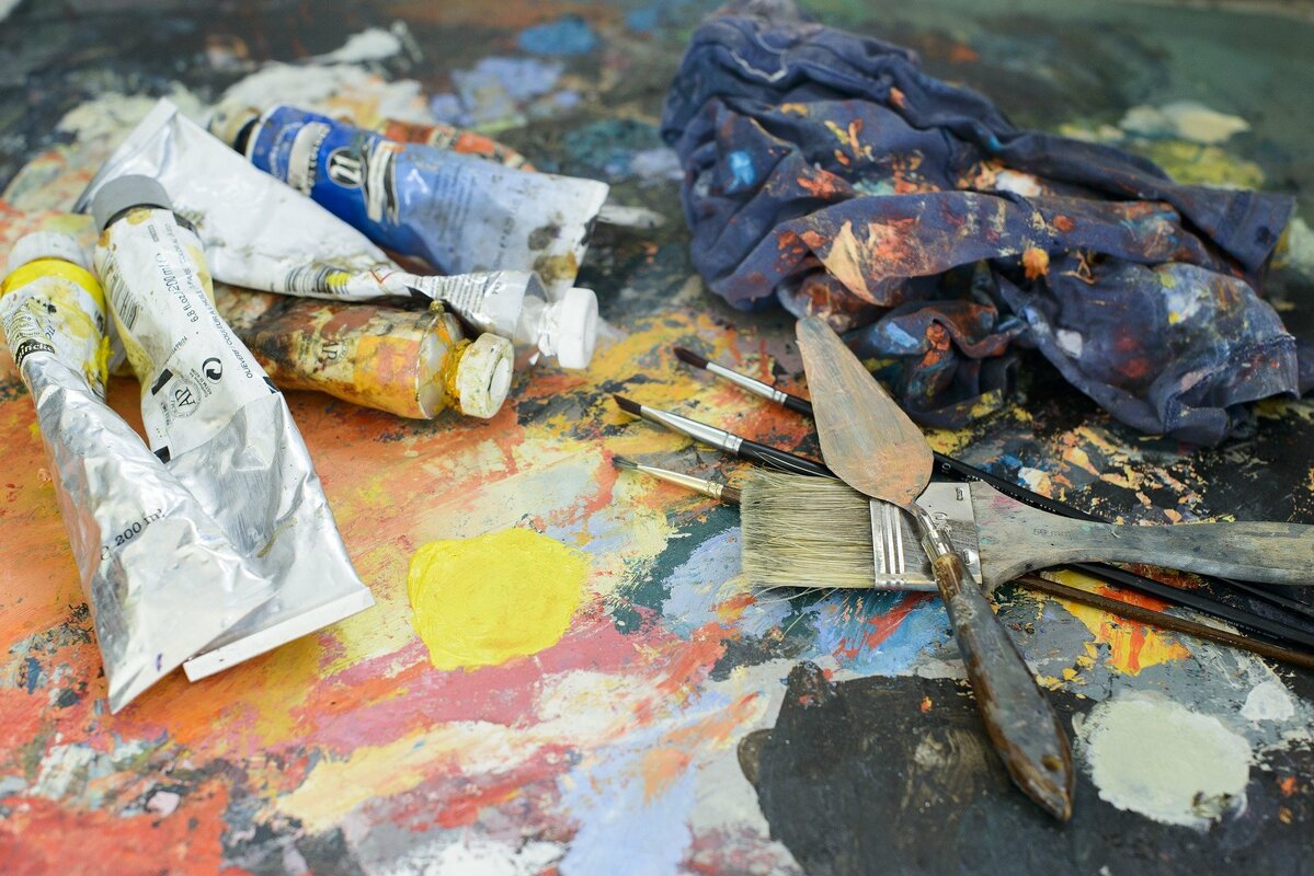 Värituubeja ja maalausvälineitä värikkäällä maalatulla taustalla.
