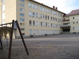 Kuvassa Keskuskoulu pihalta katsottuna: vaaleaksi rapattu nelikerroksinen koulurakennus.