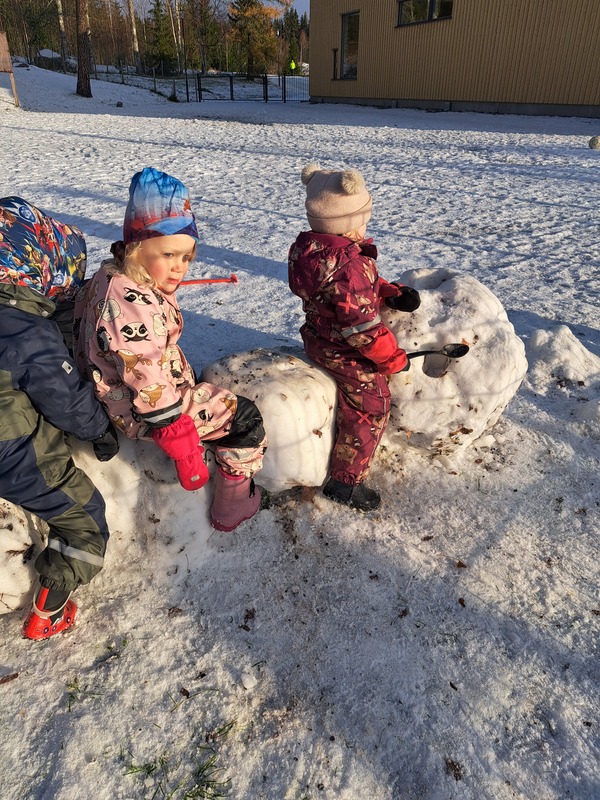Lapsia ulkona istumassa lumiteoksen päällä.