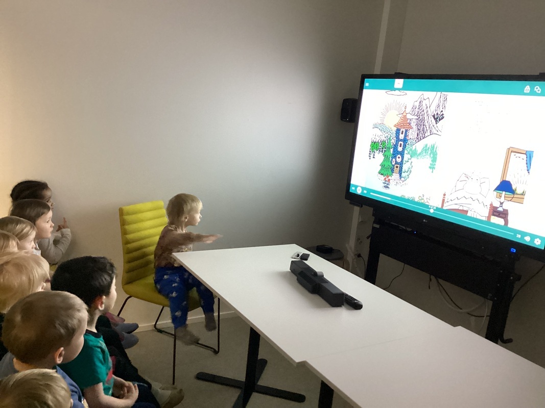 Lapsia katselemassa isolta näytöltä Muumi -kirjaa