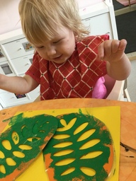 Lapsi tekee maalausta lehti sapluunalla.