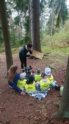 Aikuinen lukee satua metsässä ja lapset kuuntelevat tarkkaavaisina.