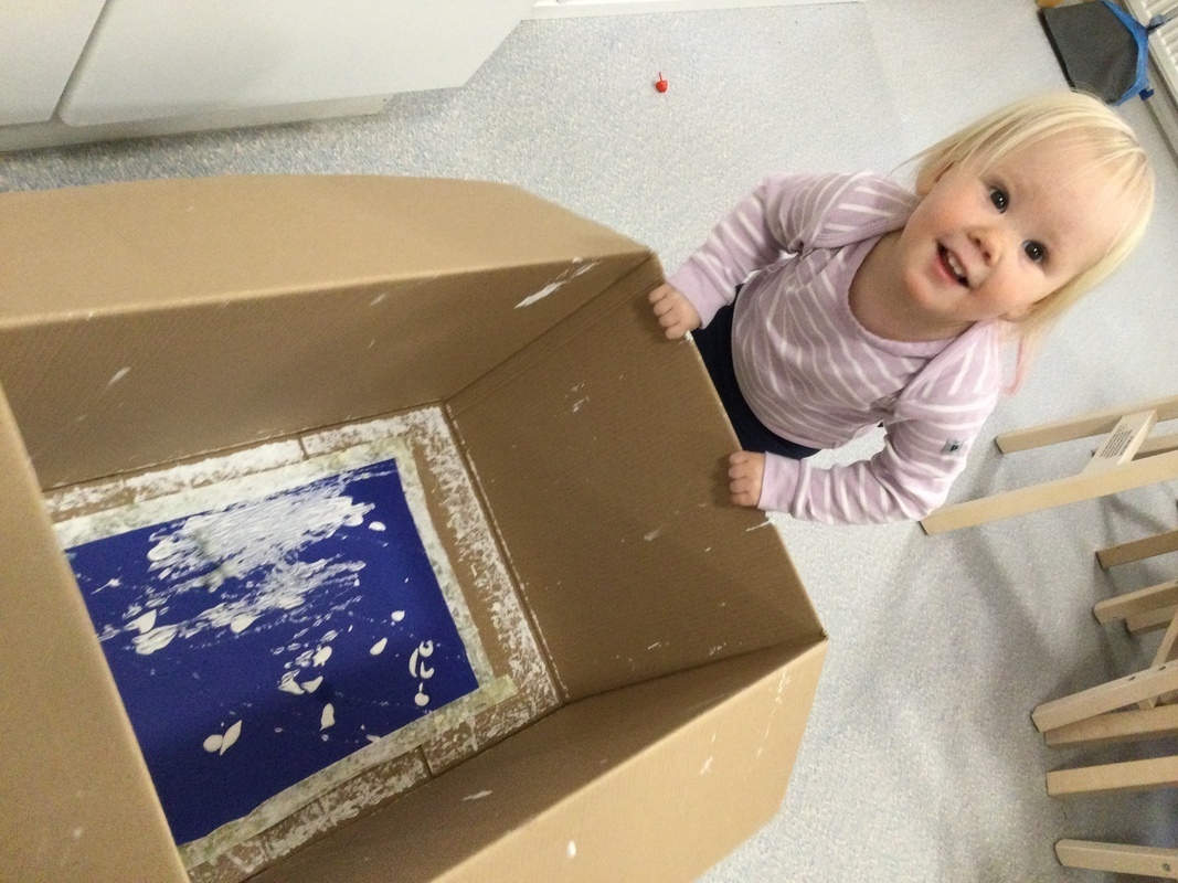 Lapsi tekee marmorimaalausta välineinään maali, laatikko ja kuula.