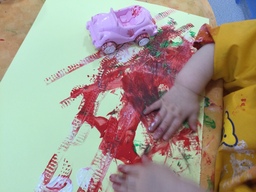 Lapsi kokeilee maalata väriä kartonkiin leikkiautolla.