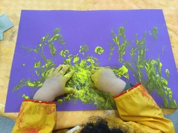 Lapsi maalaa sormilla keltaista väriä.