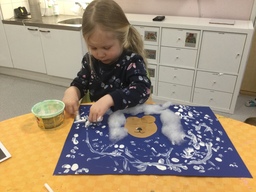Lapsi maalaa sormilla valkoisia hiutaleita nalleaskarteluun.