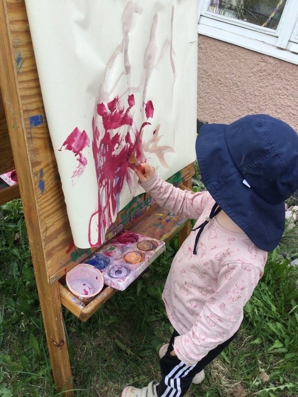 Lapsi maalaa ulkona isoon paperiin, joka on kiinnitetty maalaustelineeseen.