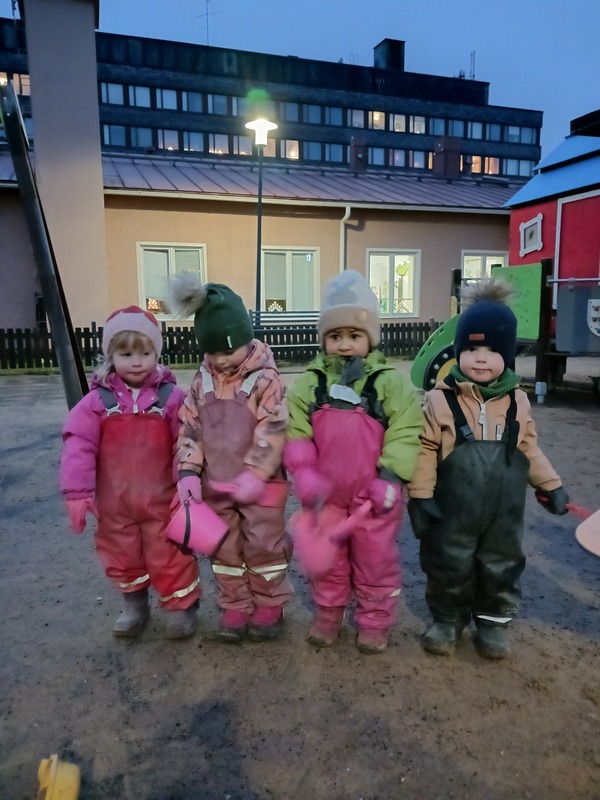 Lapset seisovat rivissä iltapäivän hämärässä päiväkodin pihalla.