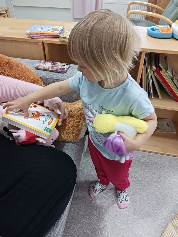 Lapsi katselee kirjaa oma lelu kainalossa.