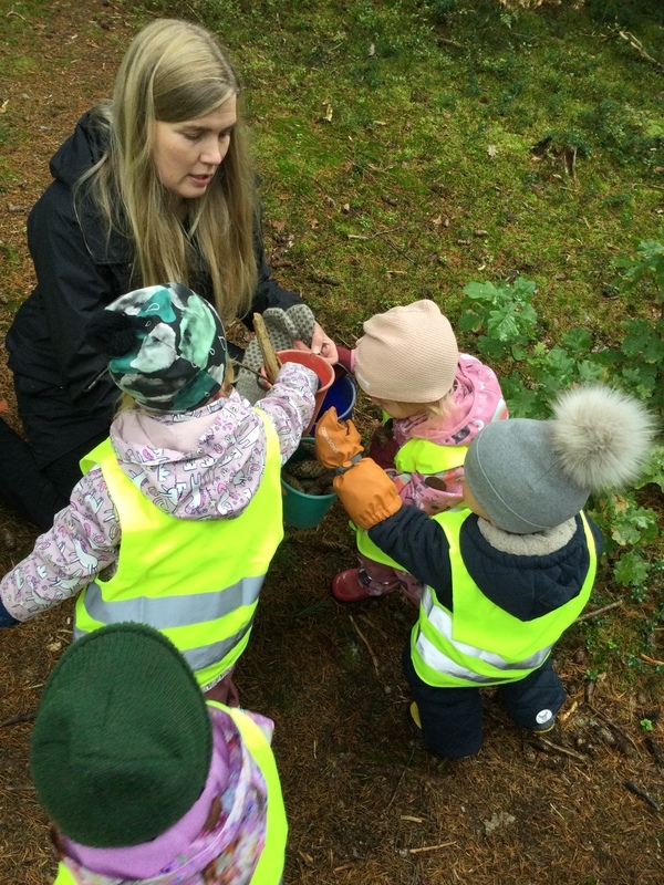 Lapset tuovat aikuiselle keräämiään metsän tuotteita.