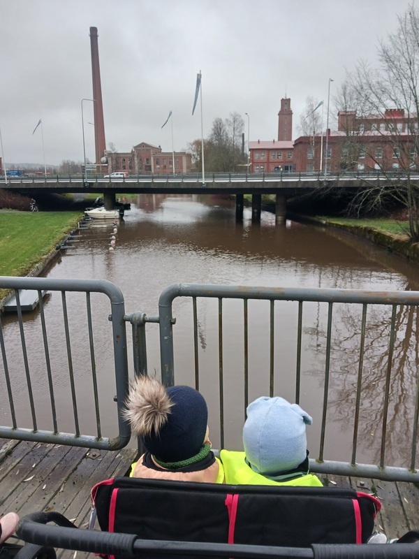 Lapset katselevat sillalla jokimaisemaa.