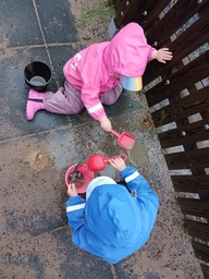 Lapset tekevät vesi hiekka kakkuja sateisena päivänä ulkona.