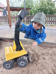 Lapsi leikkii kaivurilla hiekkalaatikolla sateisena päivänä.
