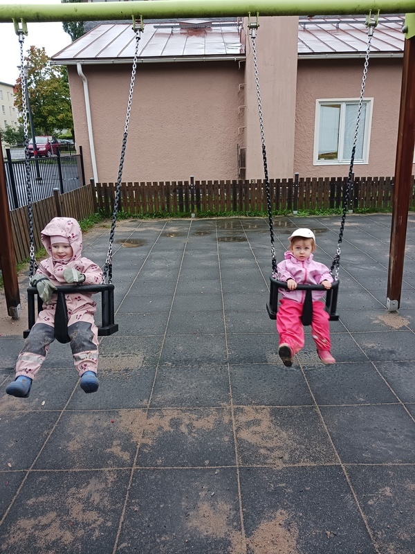 Lapset keinuvat sateisella ilmalla.