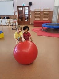 Kaksi lasta pyrittää isoa jumppapalloa salissa.