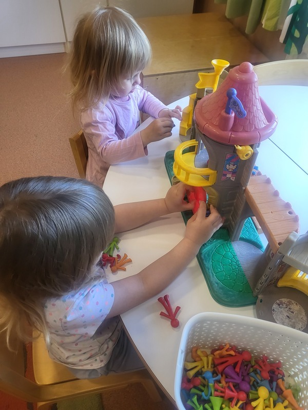 Kaksi lasta leikkii linnalla ja hahmoilla pöydän ääressä.
