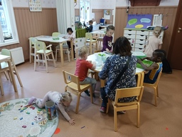Lapset leikkivät aikuisen valvonnassa pöytien ääressä.