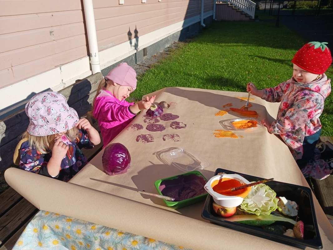 Lapset painavat maalatuilla juureksilla paperiin ulkona auringonpaisteessa.