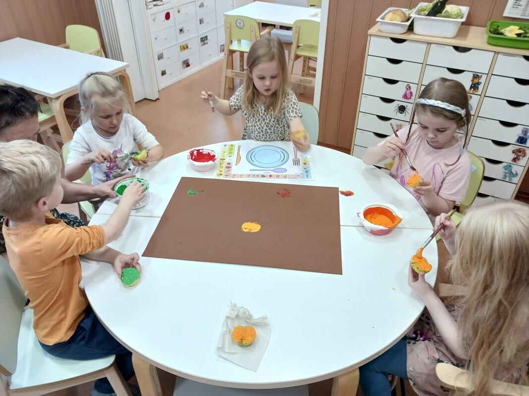 Lapset painavat omenoilla omenoiden kuvia kartonkiin.