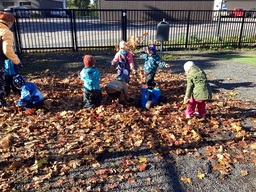 Päiväkodin pihalla lapset leikkivät lehtikasassa.