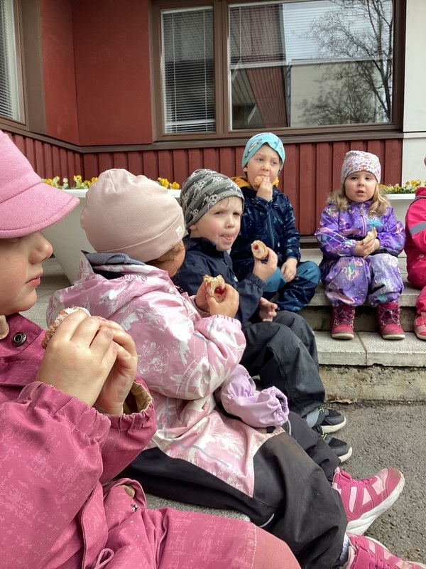 Lapset syövät munkkeja päiväkodin pihalla