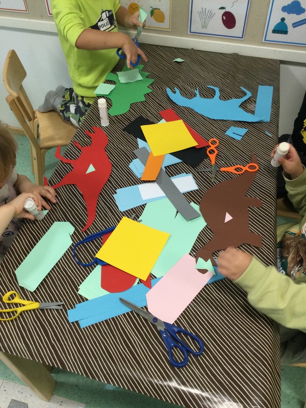 Kuvassa pöydällä eri värisiä kartonkeja, joita lapset leikkaavat saksilla