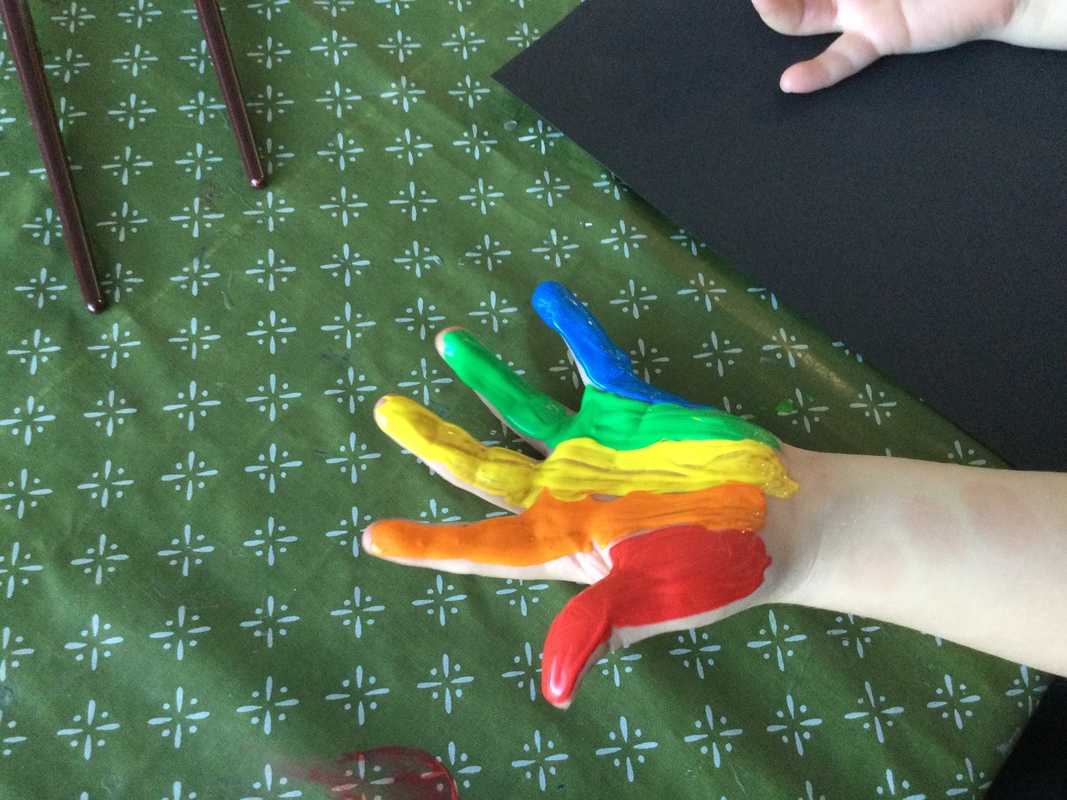 Kuvassa lapsen käsi, johon on maalattu punaisella, oranssilla, keltaisella, sinisellä ja vihreällä maalilla viivat