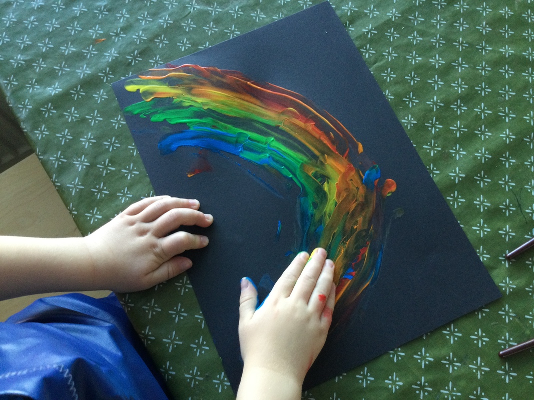 Kuvassa lapsi on kädellä maalannut sateenkaaren mustalle paperille