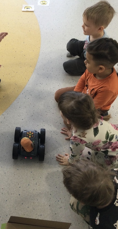 Kuvassa lattialla ohjelmoitava maastoauto, jota lapset katsovat.