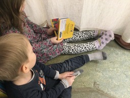 Kuvassa lapset istuvat lattialla ja lukevat kirjaa.