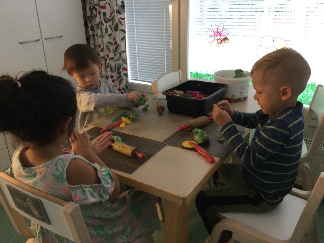 Kolme lasta muovailemaan muovailuvahoilla pöydän ääressä.