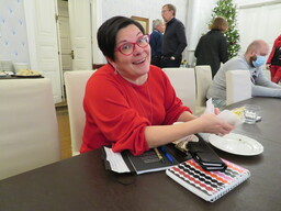 Enkeli Sari Kaasinen punaisessa mekossa salissa pöydän ääressä.