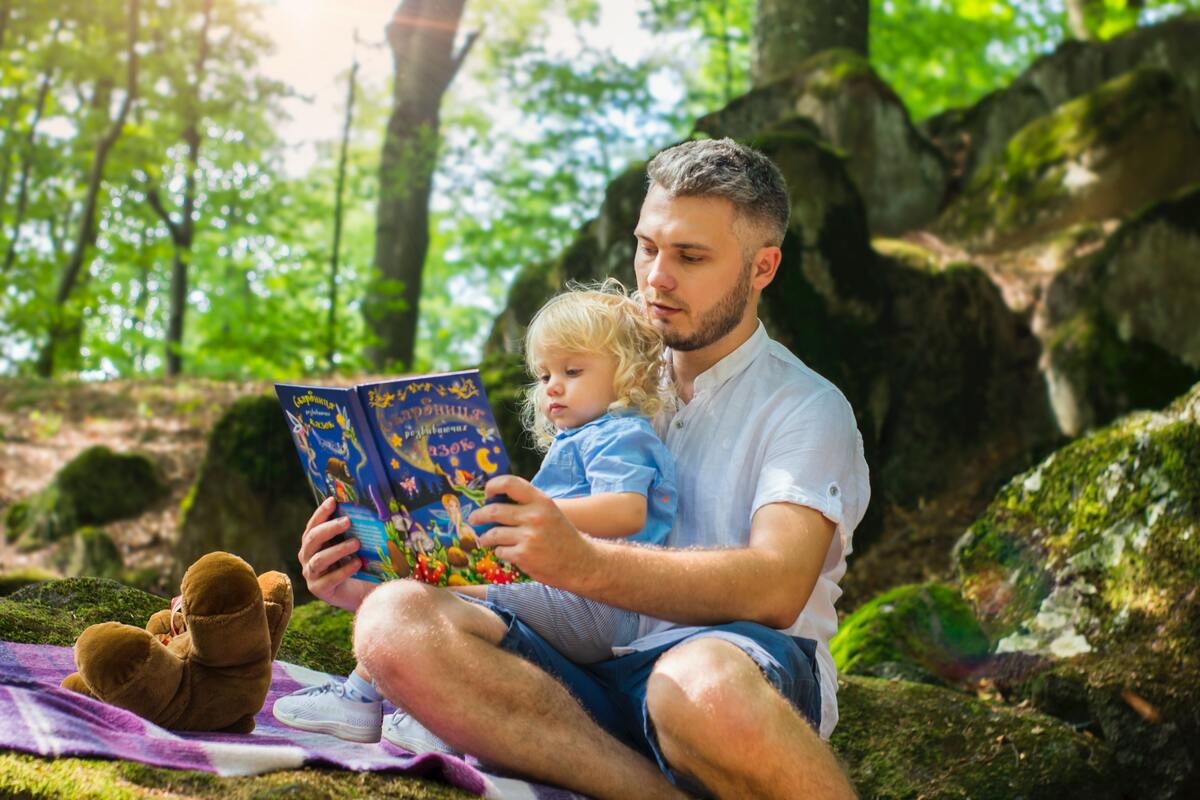 Isä ja lapsi lukevat yhdessä kirjaa metsässä.