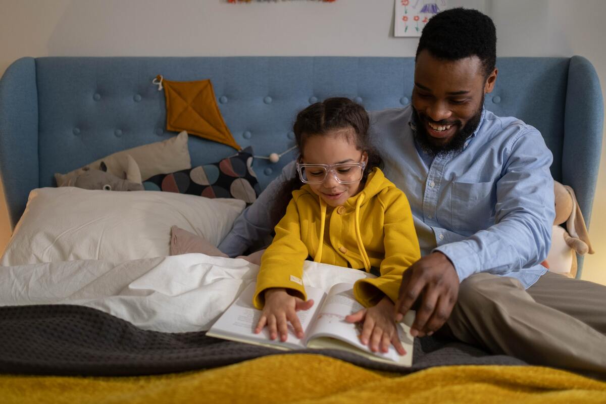 Isä ja tytär lukeva kirjaa yhdessä sängyllä. Kuvituskuva: Pexels