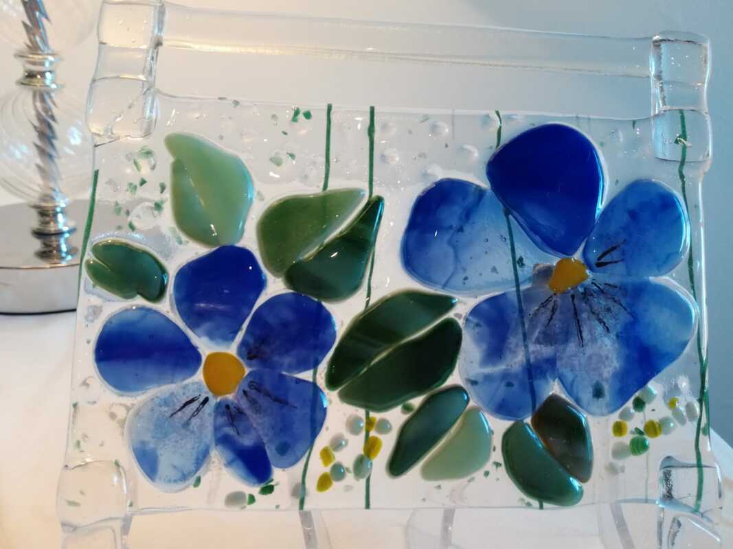 Sulatuslasitekniikalla valmistettu ikkunakoriste, jossa sinivuokkoja