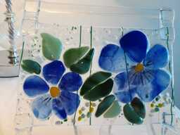 Sulatuslasitekniikalla valmistettu ikkunakoriste, jossa sinivuokkoja