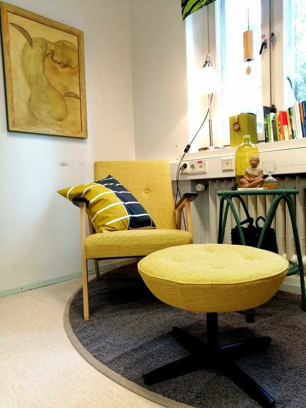 Keltaisella kankaalla verhoillut nojatuoli ja rahi