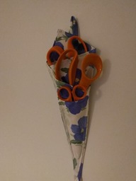 Seinälle ripustettu, sinikukkaisesta kankaasta ommeltu kotelo, jossa paikat kolmille erikokoisille saksille.