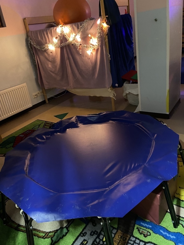 86AFDF1A-2F63-46D4-A045-9F134213AB4B.jpeg Sininen trampoliini, taustalla kerrossängyn reunalle on ripustettu valoja.