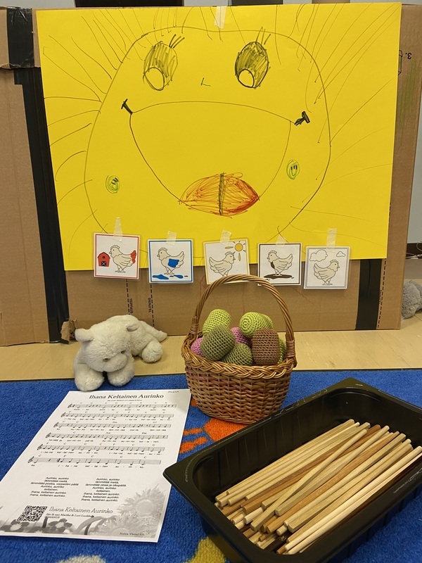 IMG_4375.jpeg Keltaiselle paperille piirretty aurinko, kuvia erivärisistä kanoista, rytmimunia ja kapuloita.