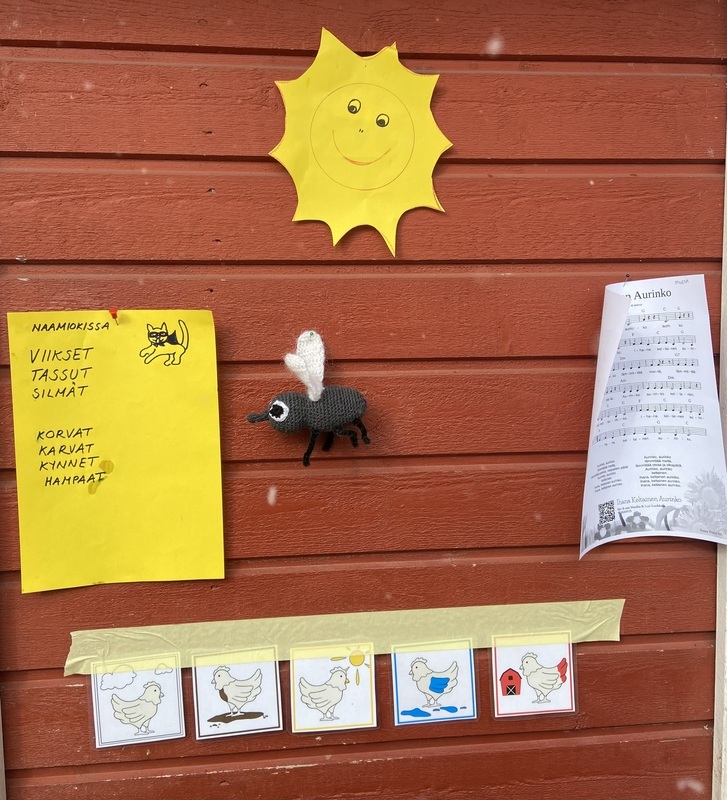 IMG_4455.jpeg Varaston punaisella seinällä kuvia eri lauluista, esim. naamiokissa, ihana keltainen aurinko ja kanapolkka.