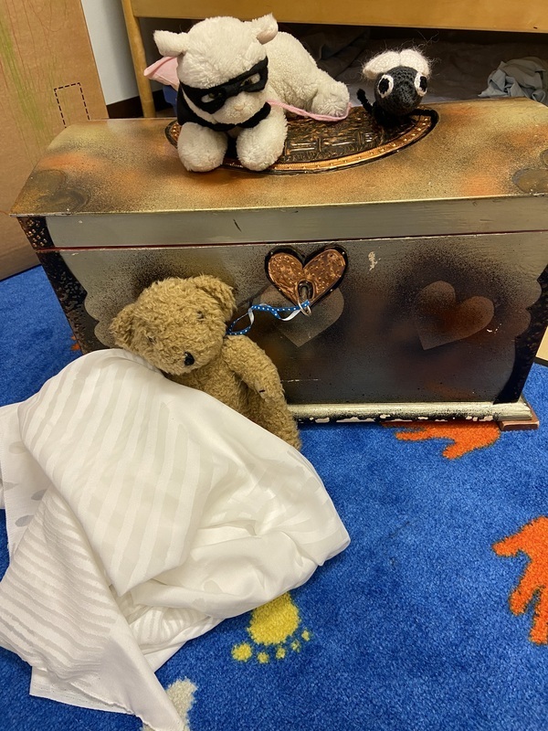 Kuva Aarrearkku ja kolme pehmolelua, nalle, valkoinen kissa naamio päässään ja virkattu kärpänen.