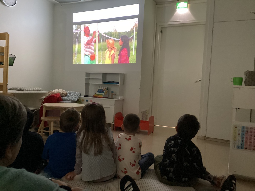 Lapset katsovat elokuvaa ja kuvassa on mies ja kaksi lasta