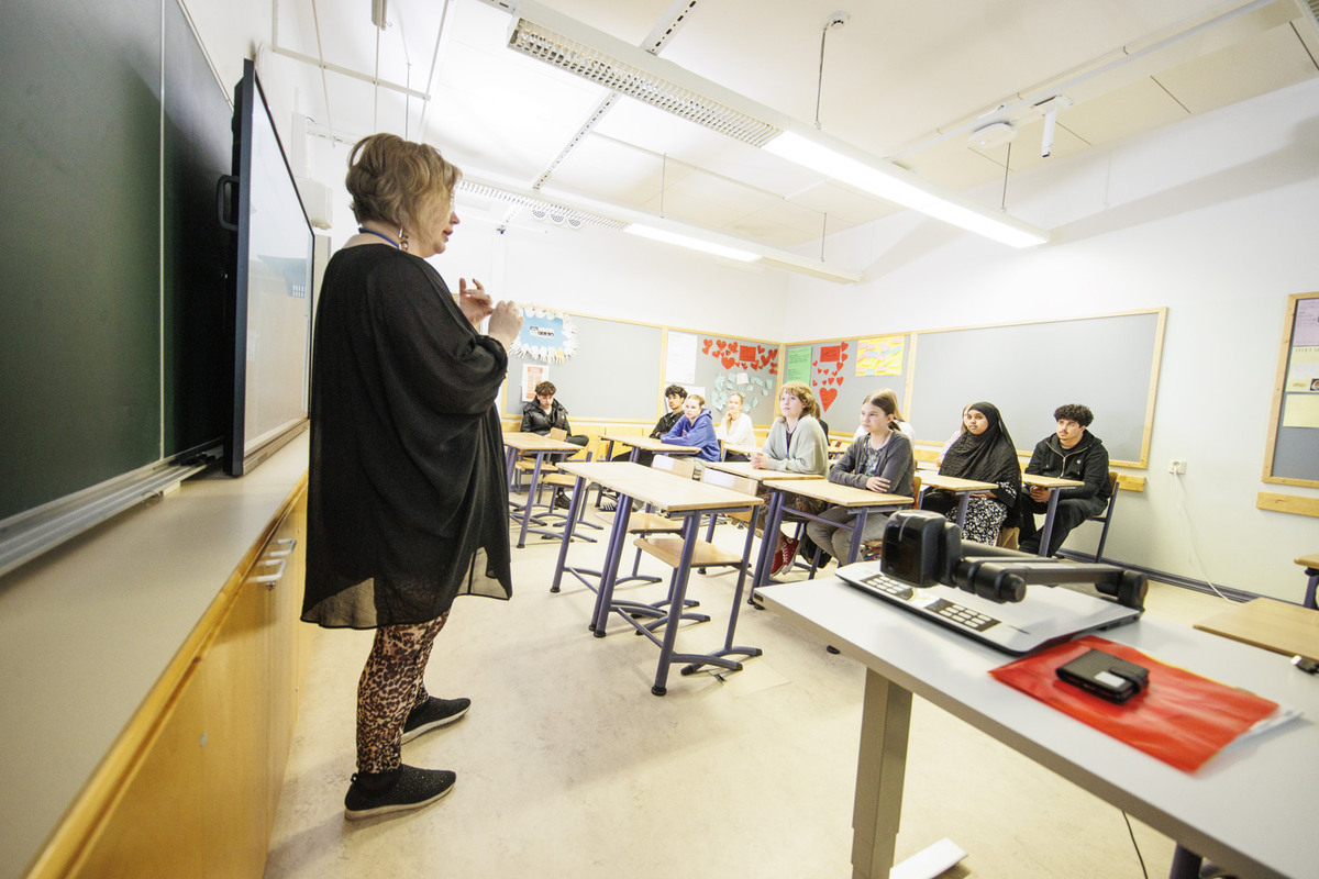 Etualalla opettaja luokkahuoneen edessä, oppilaat katsovat kohti opettajaa.