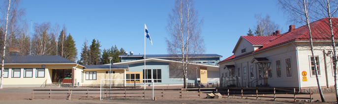 Yleiskuva uudesta ja vanhasta koulurakennuksesta. Keskellä kuvaa ja pihaa lipputangossa on Suomen lippu.