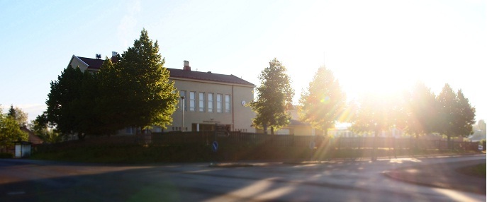 Kuvassa Saviniemen koulu kesäisessä, aurinkoisessa säässä, kuvattuna tien toiselta puolelta.