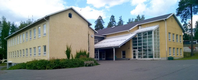Kuva Utin koulunrakennuksesta: keltaiset rapatut seinät, tummalla huovalla peitetty harjakatto, vanha osa vasemmalla ja uusi osa oikealla.